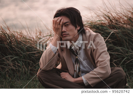 A man sitting in the grass at dusk 95620742