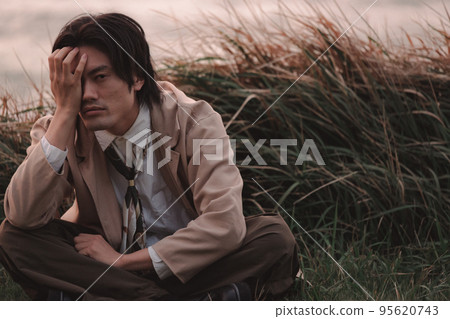 A man sitting in the grass at dusk A man sitting in the grass at dusk 95620743