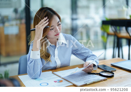 Portrait of a thoughtful Asian businesswoman looking at financial statements and making marketing plans using a computer on her desk. Portrait of a thoughtful Asian businesswoman looking at financial statements and making marketing plans using a computer on her desk. 95621208