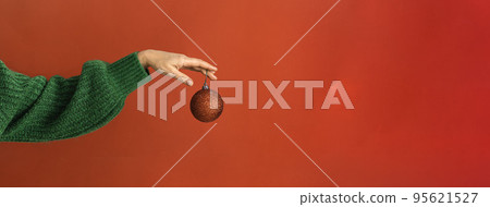 woman's hand in a green sweater holds the symbol of the New Year - a red Christmas ball. Web banner woman's hand in a green sweater holds the symbol of the New Year - a red Christmas ball. Web banner 95621527