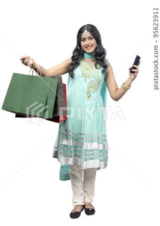 Indian woman carrying shopping bags while holding mobile phone Indian woman carrying shopping bags while holding mobile phone 95623911