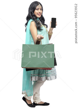 Indian woman carrying shopping bags and showing empty mobile phone screen 95623912
