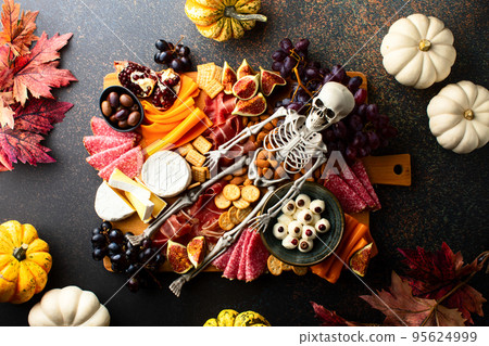 Halloween dark  table setting with cheese board decorated with spooky scary skeleton 95624999