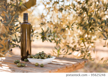 green olives and oil on table in olive grove 95625248
