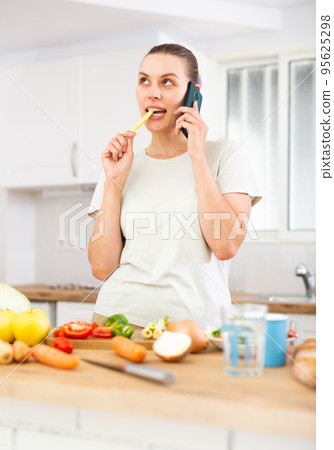 Young woman cooking dinner at home, talking on phone Young woman cooking dinner at home, talking on phone 95625298