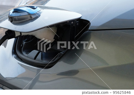 Eco friendly transport concept. Gray car is charged on electric charging station in parking lot. Close up. Loading energy. Eco friendly transport concept. Gray car is charged on electric charging station in parking lot. Close up. Loading energy. 95625846