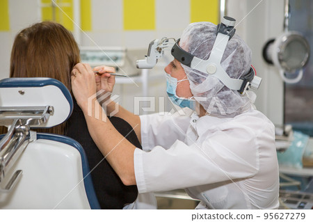 The ENT doctor, an otolaryngologist, diagnoses the ear of the patient. Wipes otitis media or ear plug. High quality photo 95627279