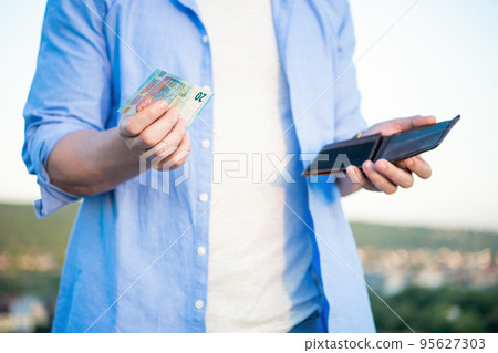 Man crop view holding money banknotes and wallet in hands outdoors Man crop view holding money banknotes and wallet in hands outdoors 95627303