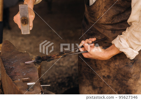 A blacksmith manually forges red-hot metal on an anvil with a hammer 95627346