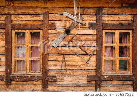 An old wooden wall of a house with windows in the village and tools hanging An old wooden wall of a house with windows in the village and tools hanging 95627538