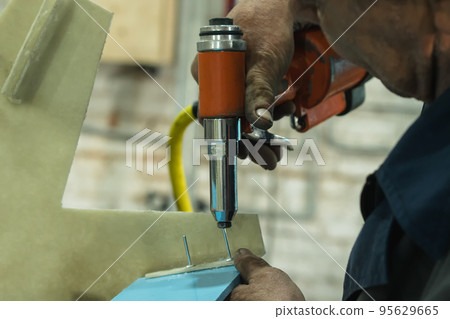 A man's hand uses a pneumatic tool to fasten parts. Riveting gun. Close-up. A worker in a pedal catamaran assembly shop. 95629665