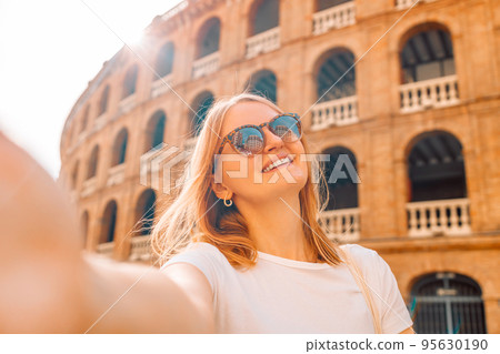 Young tourist woman in sunglasses making selfie photo on her smartphone in front of the famous Plaza de Toros de Valencia. Travel in Barcelona, Spain. Young tourist woman in sunglasses making selfie photo on her smartphone in front of the famous Plaza de Toros de Valencia. Travel in Barcelona, Spain. 95630190
