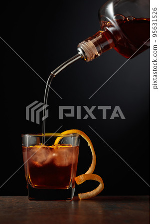 Whiskey is poured into a glass with ice and orange peel. Whiskey is poured into a glass with ice and orange peel. 95631526