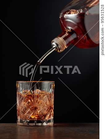 Whiskey is poured into a glass with ice. Whiskey is poured into a glass with ice. 95631528
