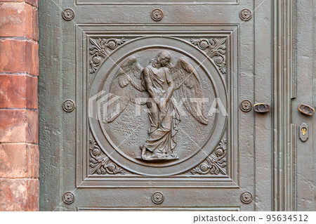 Angel carving on church doors in Berlin, Germany. Detail of the metallic panel on the temple doorway, entrance to the church. Angel carving on church doors in Berlin, Germany. Detail of the metallic panel on the temple doorway, entrance to the church. 95634512