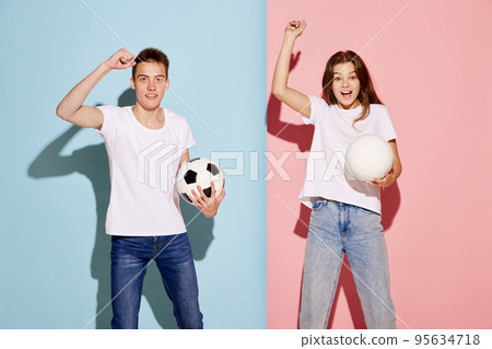 Portrait of young man and woman, sport fans posing with football ball isolated over blue-pink background. Happy Portrait of young man and woman, sport fans posing with football ball isolated over blue-pink background. Happy 95634718