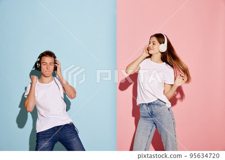 Portrait of young people, man and woman listening to music in headphones and dancing isolated over pink-blue background Portrait of young people, man and woman listening to music in headphones and dancing isolated over pink-blue background 95634720