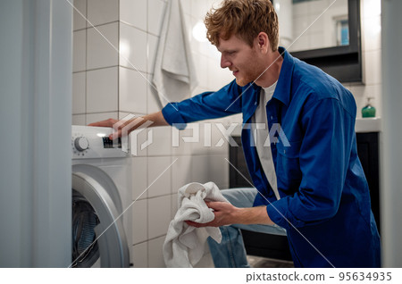 Man putting unfresh clolthes into the washing machine 95634935