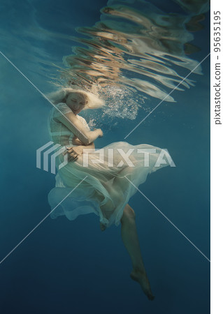 A woman with blond hair in a white dress swims underwater as if in weightlessness A woman with blond hair in a white dress swims underwater as if in weightlessness 95635195