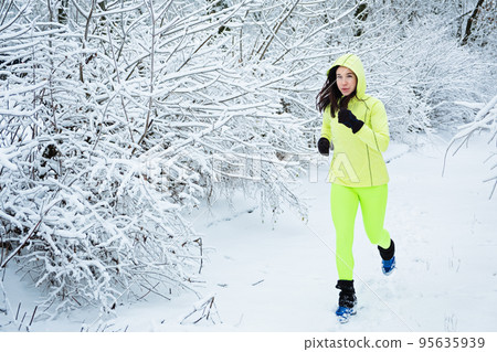 Cold Weather Running. Happy woman running in winter snowy park, forest. Running athlete woman sprinting during winter training outside in cold snow weather. Cold Weather Running. Happy woman running in winter snowy park, forest. Running athlete woman sprinting during winter training outside in cold snow weather. 95635939