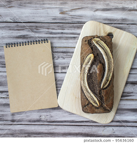 Homemade banana bread on a wooden background with a blank notepad for a recipe or name. Flat lay, top view, copy space Homemade banana bread on a wooden background with a blank notepad for a recipe or name. Flat lay, top view, copy space 95636160