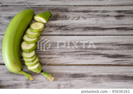 Green bananas on a wooden background. Whole banana and cut into circles. Flat lay, top view, copy space Green bananas on a wooden background. Whole banana and cut into circles. Flat lay, top view, copy space 95636161