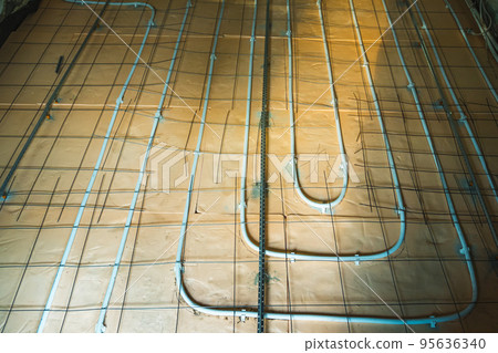 Installation of underfloor heating in a private house. Floor heating system. On the insulation rolled out the pipe for floor heating. On top lie the guides for pouring concrete. Installation of underfloor heating in a private house. Floor heating system. On the insulation rolled out the pipe for floor heating. On top lie the guides for pouring concrete. 95636340