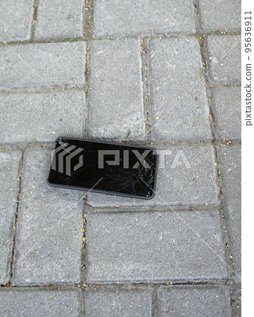 A broken smartphone lies on the road, lined with paving slabs. Cracked mobile phone screen. vertical photo A broken smartphone lies on the road, lined with paving slabs. Cracked mobile phone screen. vertical photo 95636911