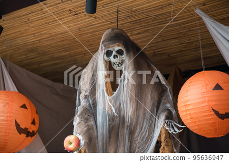 Halloween skull with white cloak hanging by smiling pumpkins Halloween skull with white cloak hanging by smiling pumpkins 95636947