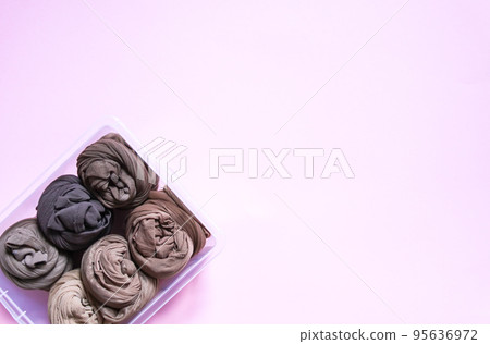 Colorful clothes vertical storage in home wardrobe. Tights in a plastic box on soft pink background 95636972