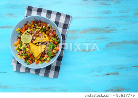 Texas caviar. Vegetable dish with corn, beans, pepper, pepper, tomatoes, beans. Served with corn chips nachos. Wooden background. Copy space Texas caviar. Vegetable dish with corn, beans, pepper, pepper, tomatoes, beans. Served with corn chips nachos. Wooden background. Copy space 95637779