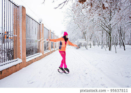 Winter workout, exercising in cold weather. Winter fitness Trening kangoo jumps. Sporty woman in sportswear and kangoo jump shoes jumping in winter snowy park, forest. 95637811