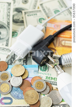 The concept of the energy crisis, price increases. Euro and dollar banknotes, coins on the background of a lamp, plug, cord. Tax time, bill payment, calculator for counting. Vertical photo. 95637890