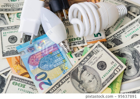 The concept of the energy crisis, price increases. Euro and dollar banknotes, coins on the background of a lamp, plug, cord. Tax time, bill payment, calculator for counting. 95637891