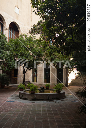 Street view with a fountain of green plants and orange trees around in a cozy courtyard. Valencia, Spain 95639837