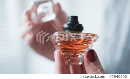 Perfume bottle in a female hand against the background of light room interior. Perfume bottle in a female hand against the background of light room interior. 95640200