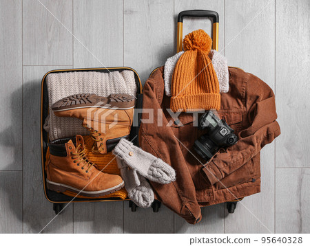 Open suitcase with warm clothes and camera on wooden floor, flat lay. Winter vacation 95640328