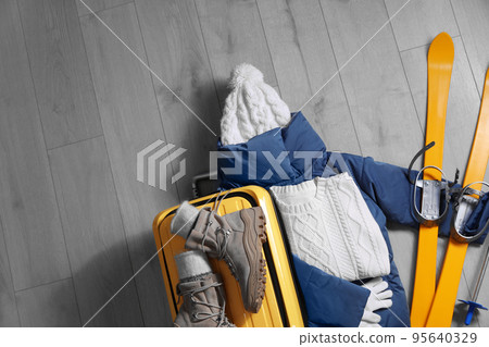 Suitcase with warm clothes and skis on wooden floor, flat lay. Winter vacation 95640329