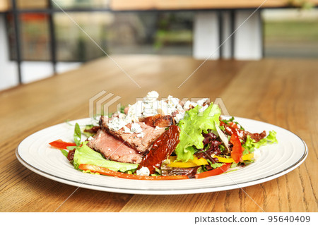 Delicious salad with roasted meat and vegetables served on wooden table indoors. Space for text 95640409