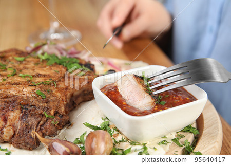 Woman eating delicious grilled pork chop at wooden table, closeup Woman eating delicious grilled pork chop at wooden table, closeup 95640417