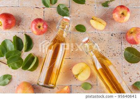Apple cider vinegar in a two glass bottles and fresh apples with leaves on beige concrete background, top view, close up Apple cider vinegar in a two glass bottles and fresh apples with leaves on beige concrete background, top view, close up 95640641