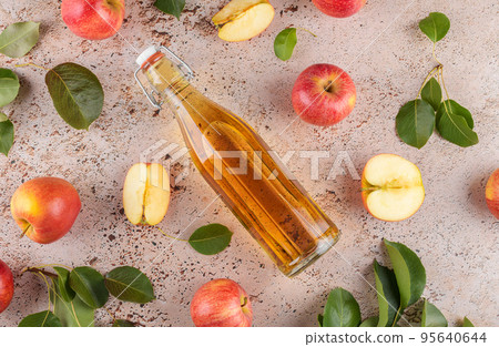 Apple cider vinegar in a glass bottle and fresh apples with leaves on beige concrete background, top view, close up 95640644