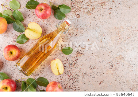 Apple cider vinegar in a glass bottle and fresh apples with leaves on beige concrete background, top view, flat lay Apple cider vinegar in a glass bottle and fresh apples with leaves on beige concrete background, top view, flat lay 95640645