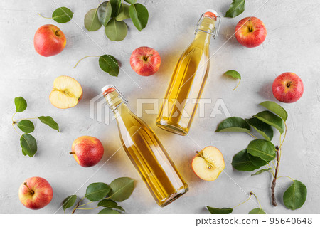 Apple cider vinegar in a two glass bottles and fresh apples with leaves on light background, top view, flat lay Apple cider vinegar in a two glass bottles and fresh apples with leaves on light background, top view, flat lay 95640648