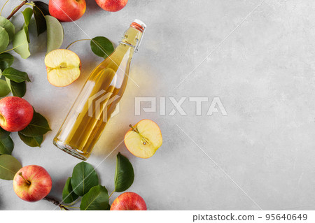 Apple cider vinegar in a glass bottle and fresh apples with leaves on light background, top view, flat lay Apple cider vinegar in a glass bottle and fresh apples with leaves on light background, top view, flat lay 95640649