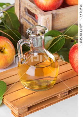 Apple cider vinegar in a glass bottle and fresh apples with leaves on light background Apple cider vinegar in a glass bottle and fresh apples with leaves on light background 95640650