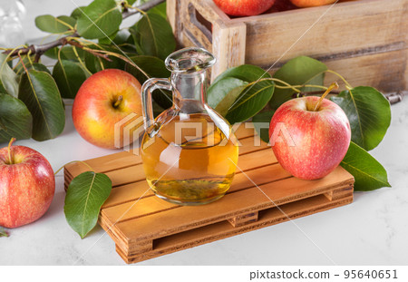 Apple cider vinegar in a glass bottle and fresh apples with leaves on light background Apple cider vinegar in a glass bottle and fresh apples with leaves on light background 95640651