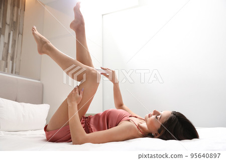 Young woman epilating her legs in bedroom 95640897