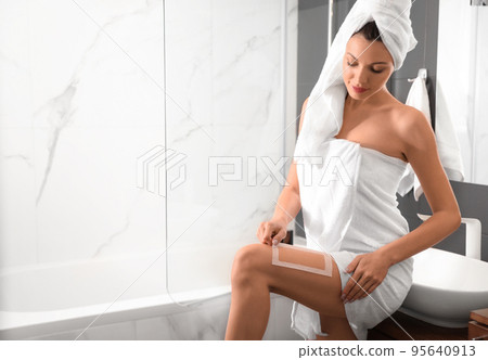 Young woman waxing her legs in bathroom. Epilation procedure 95640913