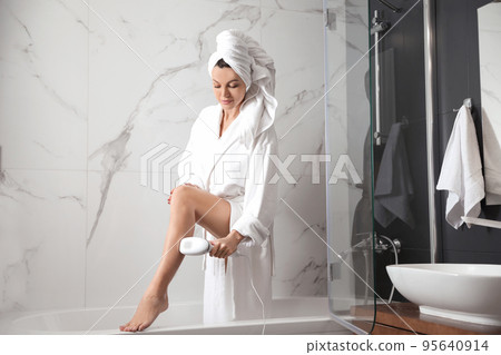 Young woman epilating her legs in bathroom 95640914